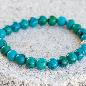 May include: A turquoise gemstone bracelet with silver beads. The bracelet is made of round beads and is strung on a stretchy cord.