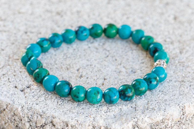 May include: A turquoise gemstone bracelet with silver beads. The bracelet is made of round beads and is strung on a stretchy cord.