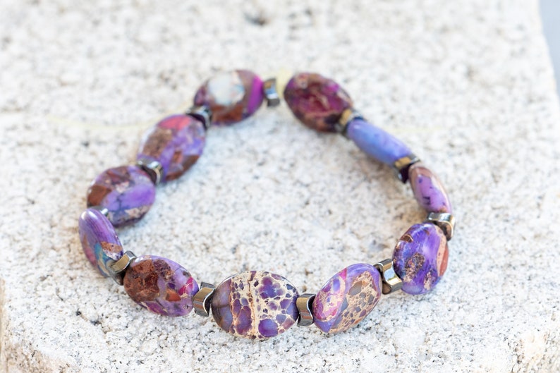 May include: A purple and brown gemstone bracelet with silver accents. The bracelet is made of oval-shaped stones and is strung on a silver chain.
