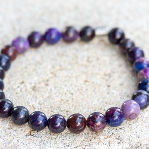 May include: A purple and black beaded bracelet with a silver clasp. The beads are round and have a smooth, polished finish.