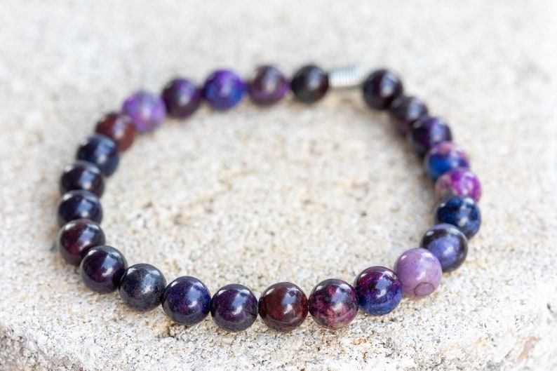 May include: A purple and black beaded bracelet with a silver clasp. The beads are round and have a smooth, polished finish.