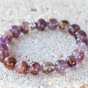 May include: A purple and brown gemstone bracelet with a silver clasp. The bracelet is made of round beads and is approximately 7 inches in length.