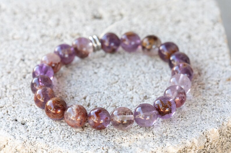 May include: A purple and brown gemstone bracelet with a silver clasp. The bracelet is made of round beads and is approximately 7 inches in length.