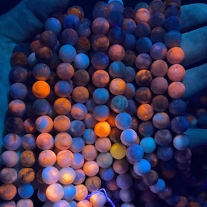 May include: A strand of round, multi-colored beads with a blue, orange, and yellow color scheme. The beads are made of a translucent material that glows under a black light.