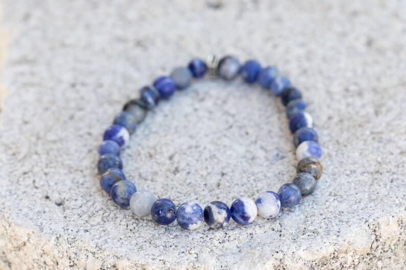 May include: A blue and white gemstone bracelet with a silver clasp. The bracelet is made of round beads and is approximately 7 inches in length.