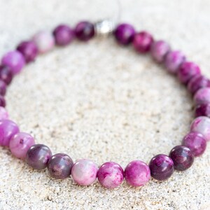 May include: A purple and pink gemstone bracelet with a silver clasp. The bracelet is made of round beads with a gradient of color from light pink to dark purple.