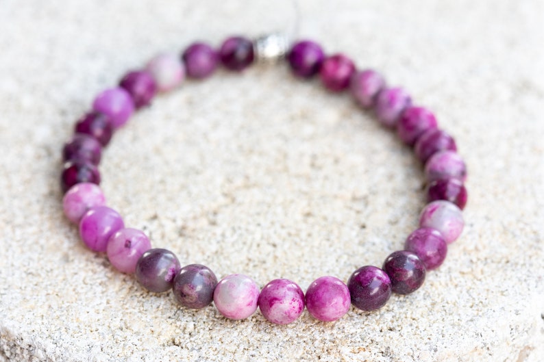 May include: A purple and pink gemstone bracelet with a silver clasp. The bracelet is made of round beads with a gradient of color from light pink to dark purple.
