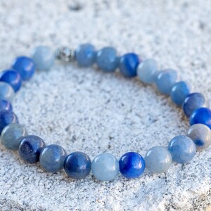 May include: A blue gemstone bracelet with beads of varying shades of blue, from light to dark. The bracelet is made with round beads and has a silver clasp.