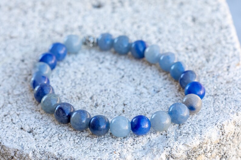 May include: A blue gemstone bracelet with beads of varying shades of blue, from light to dark. The bracelet is made with round beads and has a silver clasp.