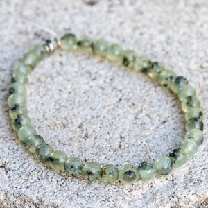 May include: A green and black gemstone bracelet with a silver clasp. The bracelet is made of round beads and is approximately 7 inches in length.