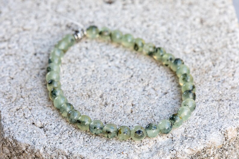 May include: A green and black gemstone bracelet with a silver clasp. The bracelet is made of round beads and is approximately 7 inches in length.