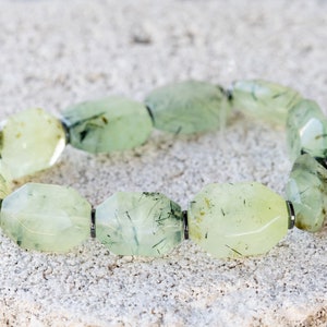May include: A green aventurine bracelet with faceted beads and silver accents. The beads are a light green color with dark green inclusions.