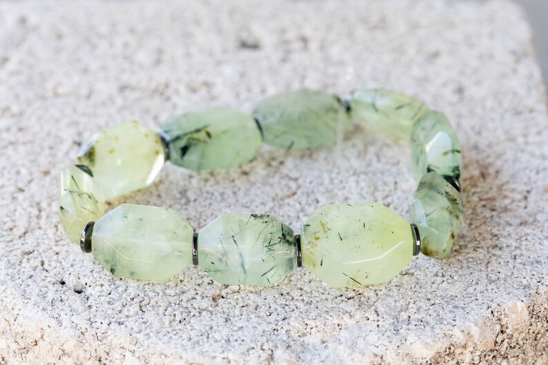 May include: A green aventurine bracelet with faceted beads and silver accents. The beads are a light green color with dark green inclusions.