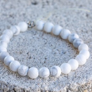 Może przedstawiać: Bransoletka z białych koralik&oacute;w howlitowych z srebrnym zapięciem. Korale są okrągłe i mają gładkie, polerowane wykończenie.