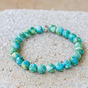 May include: A turquoise and green gemstone bracelet with silver accents. The bracelet is made of round beads and is strung on a silver chain.