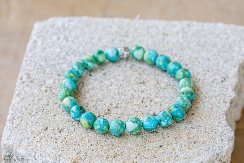 May include: A turquoise and green gemstone bracelet with silver accents. The bracelet is made of round beads and is strung on a silver chain.