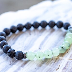 May include: A black lava rock and green jade beaded bracelet. The bracelet is made with round beads and a silver metal clasp.