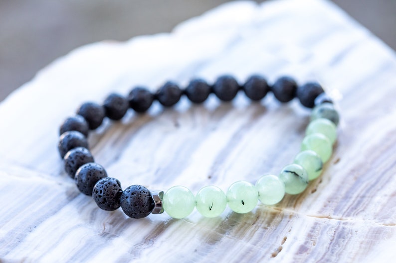 May include: A black lava rock and green jade beaded bracelet. The bracelet is made with round beads and a silver metal clasp.