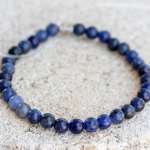 May include: A blue gemstone bracelet with a silver clasp. The bracelet is made of round beads and is approximately 7 inches in length.
