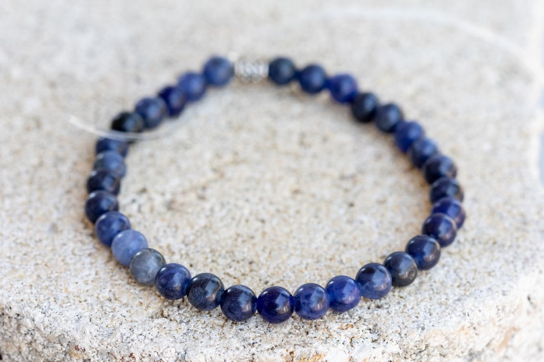 May include: A blue gemstone bracelet with a silver clasp. The bracelet is made of round beads and is approximately 7 inches in length.