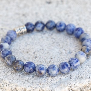 May include: A blue and white gemstone bracelet with a silver clasp. The bracelet is made of round beads and is approximately 7 inches in length.