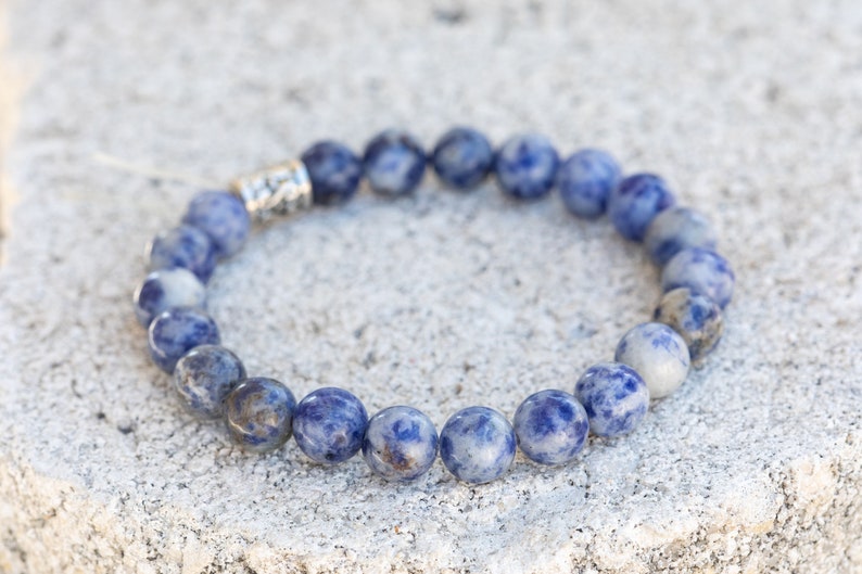 May include: A blue and white gemstone bracelet with a silver clasp. The bracelet is made of round beads and is approximately 7 inches in length.