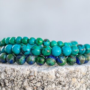 May include: Three stacked bracelets made of blue and green gemstone beads. The beads are round and have a smooth, polished finish.