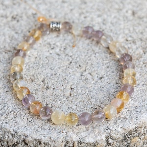 May include: A beaded bracelet featuring a mix of light purple, yellow, and clear beads. The bracelet has a silver clasp.