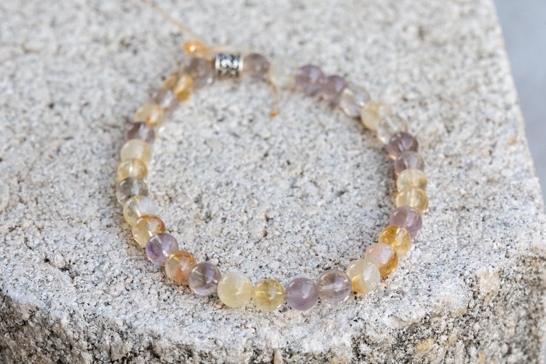 May include: A beaded bracelet featuring a mix of light purple, yellow, and clear beads. The bracelet has a silver clasp.