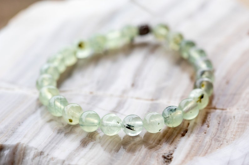 May include: A green gemstone bracelet with a silver clasp. The bracelet is made of round beads with black and green inclusions.