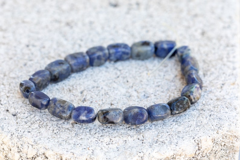 May include: A bracelet made of blue and white lapis lazuli beads. The beads are rectangular and have a smooth, polished finish.