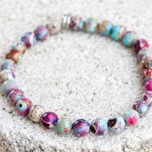 May include: A bracelet made of colorful, round, multi-colored jasper beads. The beads are a mix of pink, purple, blue, and brown.