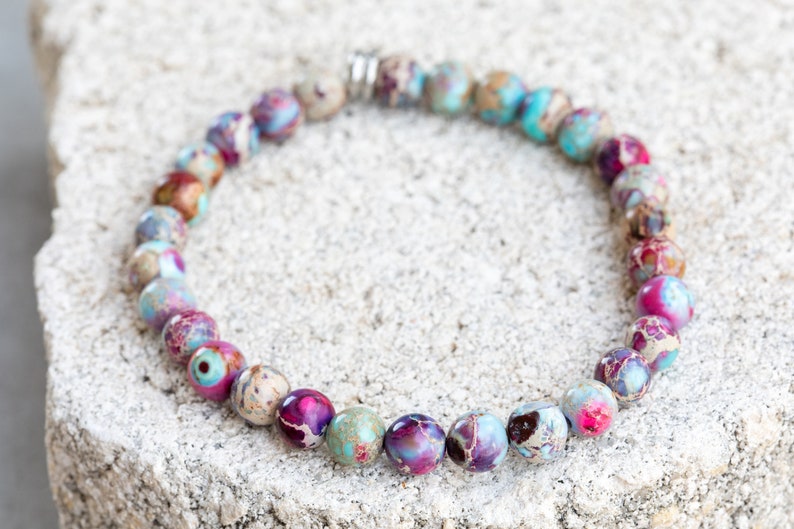 May include: A bracelet made of colorful, round, multi-colored jasper beads. The beads are a mix of pink, purple, blue, and brown.