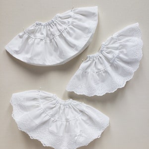 May include: Three white cotton petticoats with lace trim. The petticoats are layered and have a ruffled design.