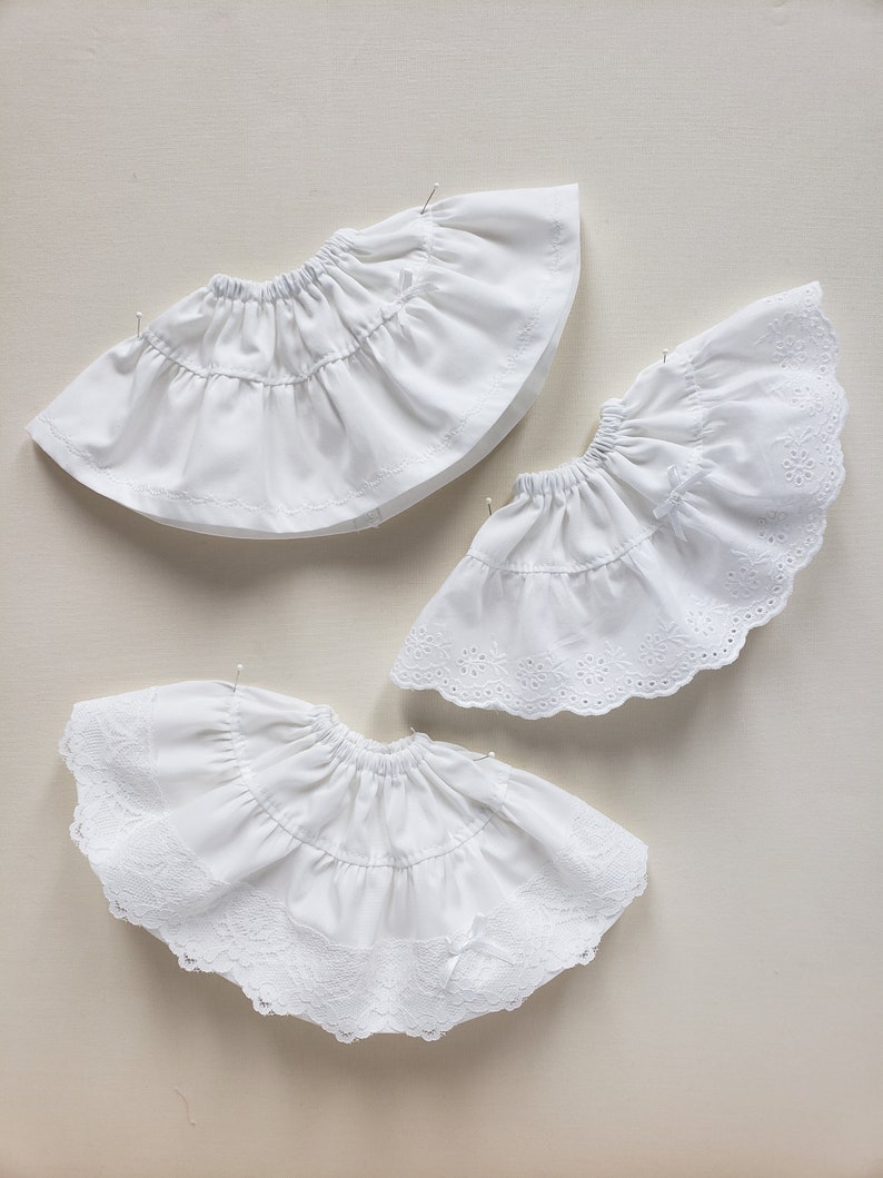 May include: Three white cotton petticoats with lace trim. The petticoats are layered and have a ruffled design.