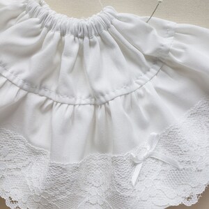 May include: White cotton skirt with a lace trim and a bow. The skirt has a gathered elastic waistband.