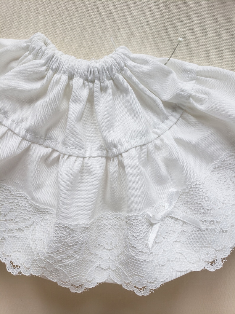 May include: White cotton skirt with a lace trim and a bow. The skirt has a gathered elastic waistband.