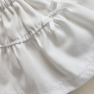 May include: White cotton skirt with a white satin bow at the waist. The skirt has a ruffled hem and is made of a soft, lightweight fabric.