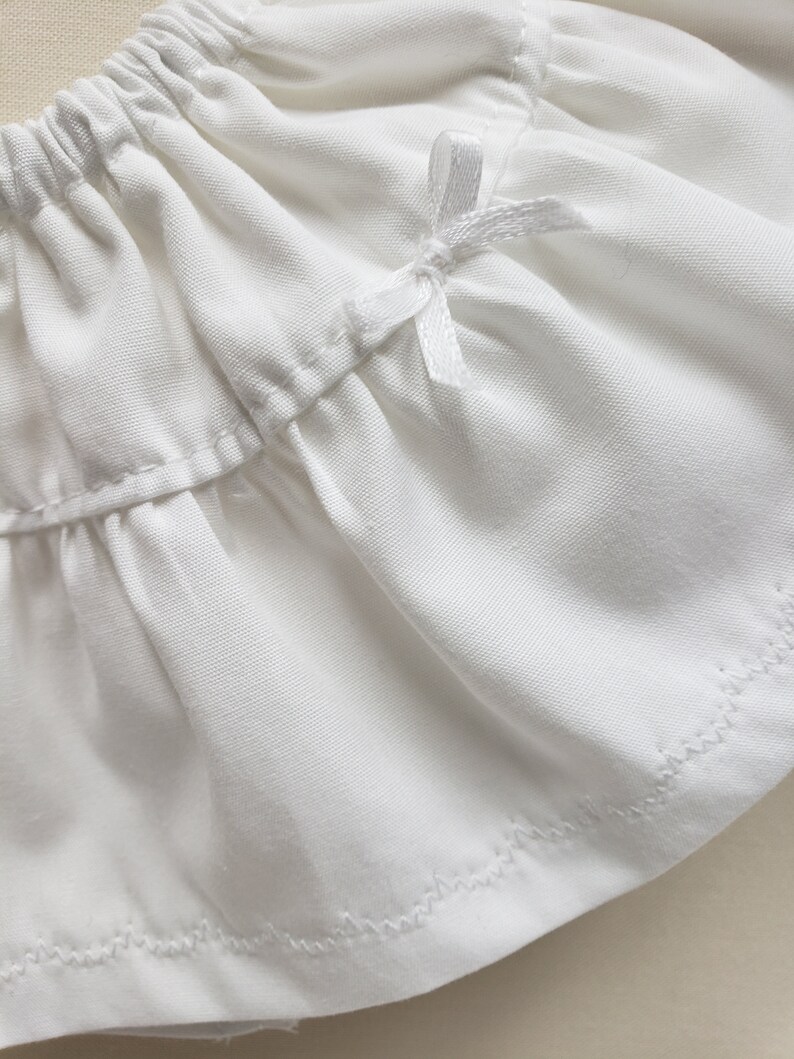 May include: White cotton skirt with a white satin bow at the waist. The skirt has a ruffled hem and is made of a soft, lightweight fabric.