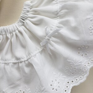 May include: White cotton fabric with a ruffled edge and eyelet lace trim. The fabric has a delicate, feminine feel.