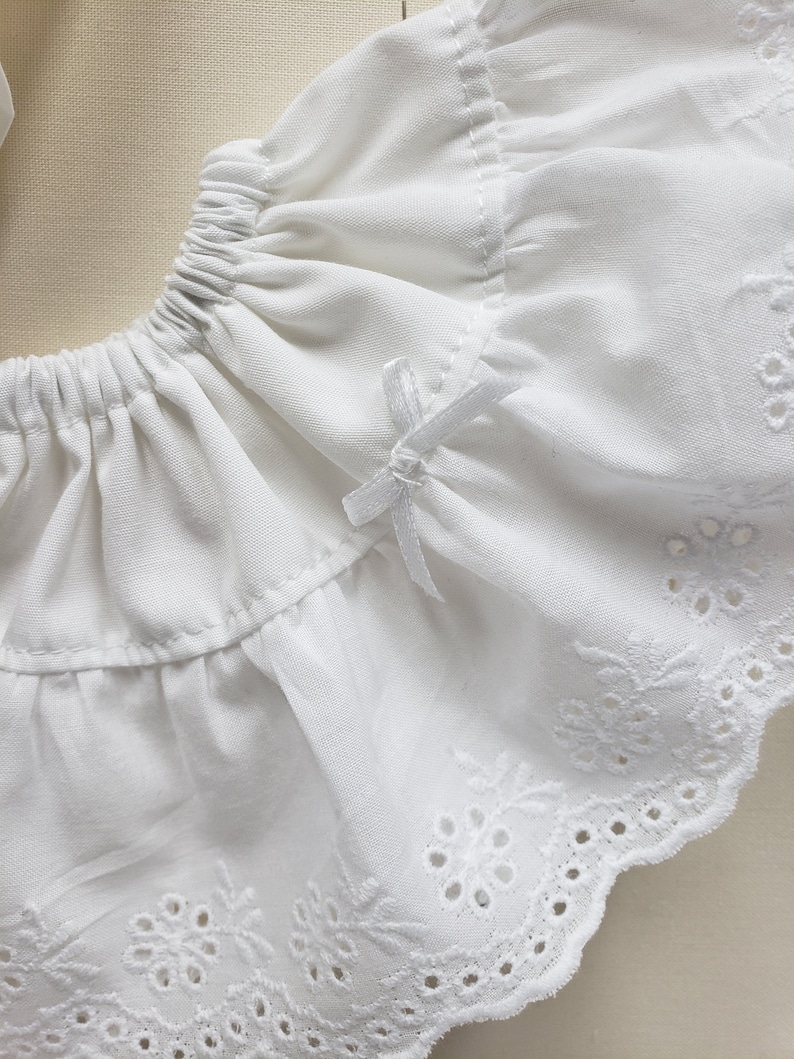 May include: White cotton fabric with a ruffled edge and eyelet lace trim. The fabric has a delicate, feminine feel.
