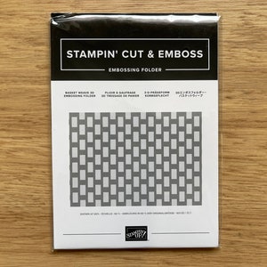 May include: A white card with black text that reads "Stampin' Cut & Emboss Embossing Folder" and shows a black and white image of a basket weave pattern. The text also reads "Basket Weave 3D Embossing Folder" in English, French, German, and Japanese.