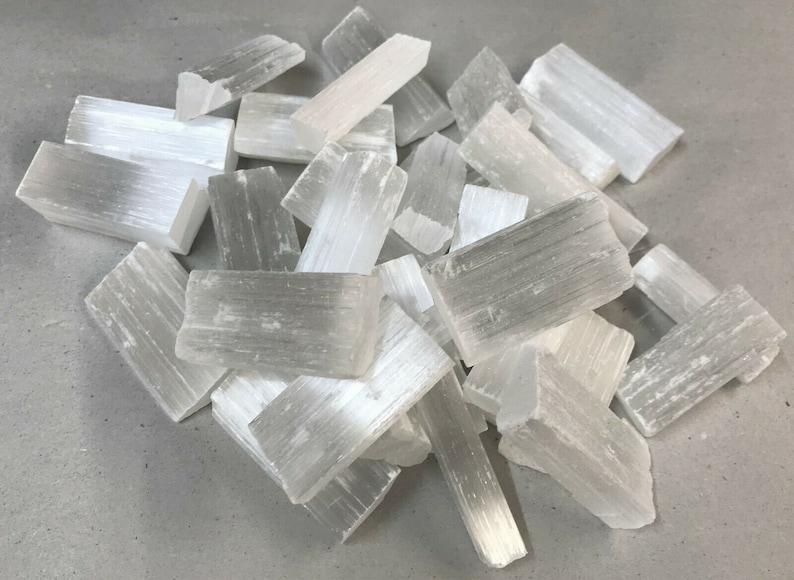 May include: A pile of white selenite crystal sticks. The sticks are rough and have a natural, unpolished look.
