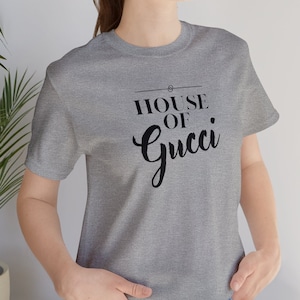 May include: A gray t-shirt with black text that reads "HOUSE OF Gucci" in a cursive font.