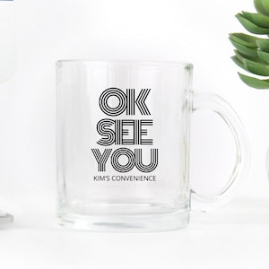 May include: A clear glass mug with a black graphic that says "OK SEE YOU" and "KIM'S CONVENIENCE" underneath.
