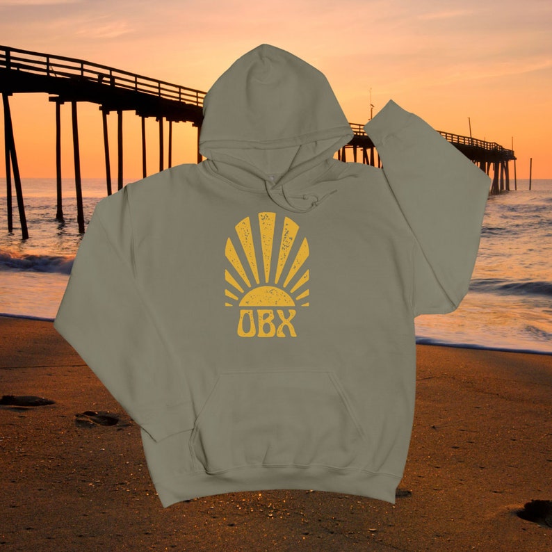 May include: A sage green hooded sweatshirt with a yellow sunburst graphic and the text "OBX" in a vintage style.