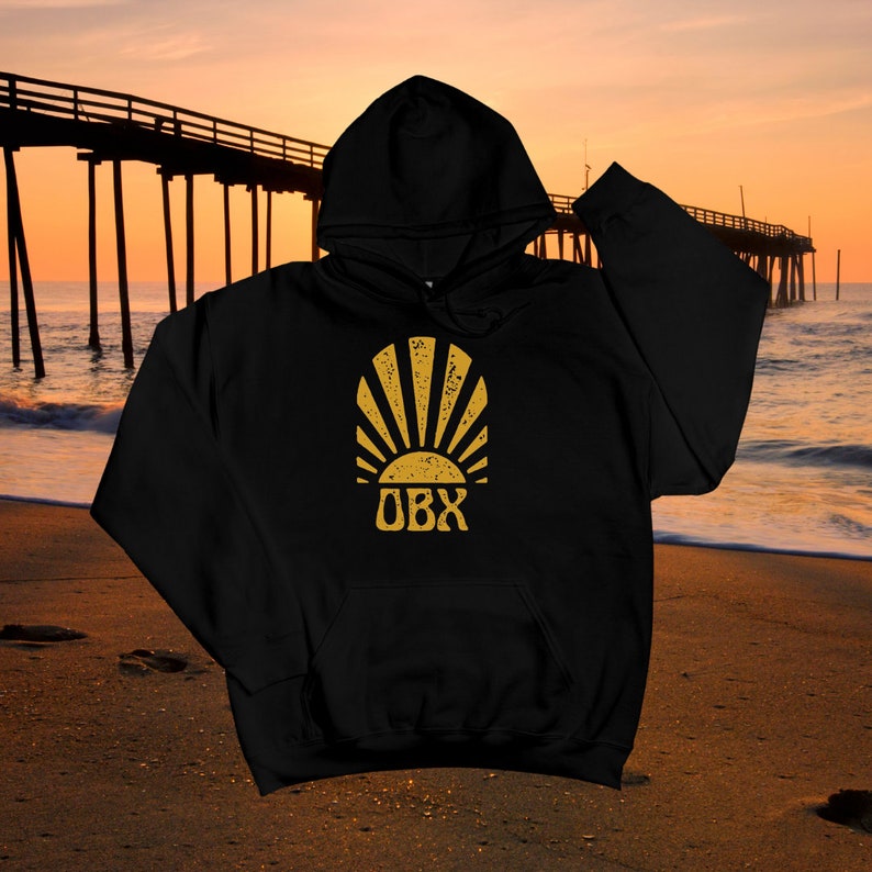 May include: Black hooded sweatshirt with a gold sun and "OBX" text on the front. The sun has a distressed look and is set against a beach background.