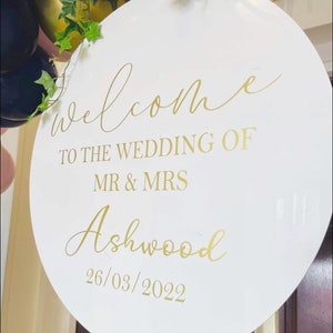 May include: White round sign with gold lettering that says "Welcome to the wedding of Mr & Mrs Ashwood 26/03/2022".