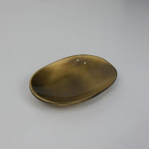 May include: A small, oval-shaped dish made of brass with a brushed finish. The dish is a light gold colour.