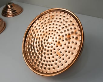 May include: A copper shower head with a hammered finish and a circular design. The shower head has many small holes for water to flow through.